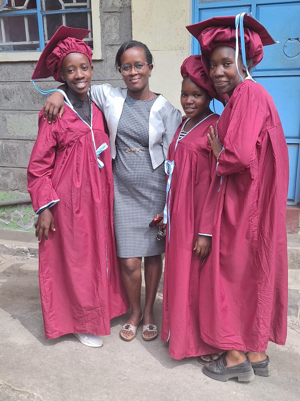 Three OnCourse students in graduation gowns with a staff member in Kenya
